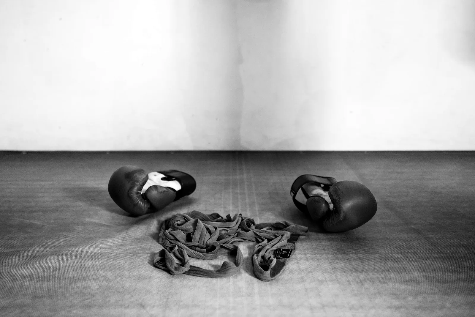 A pair of boxing gloves and a hand wrap on a gym floor, in black and white.
