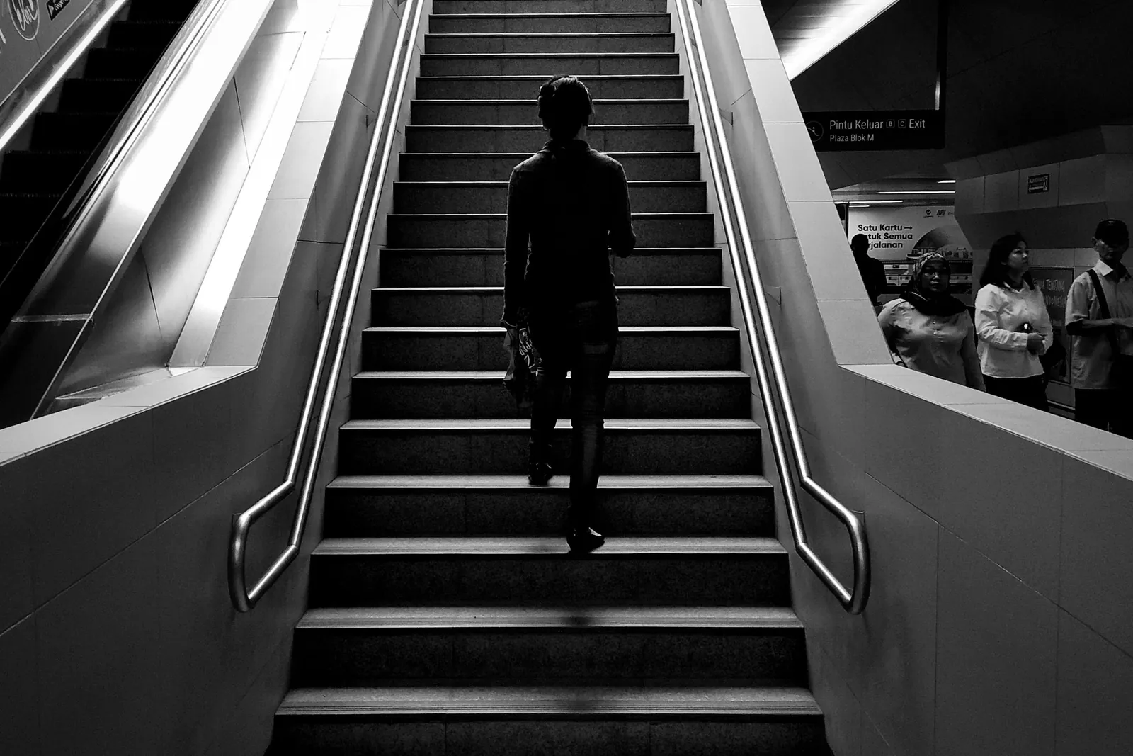 A lone figure climbing a long staircase toward the light, in black and white.