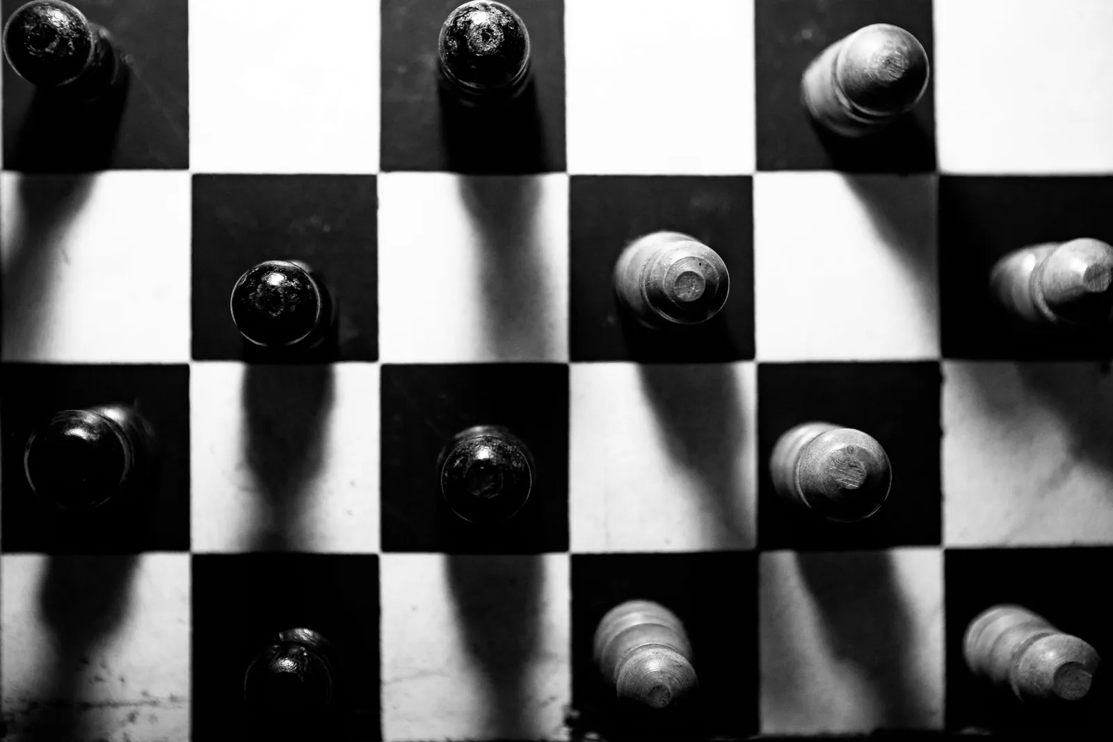 Chess pieces casting long shadows across a black and white chessboard, seen from above.