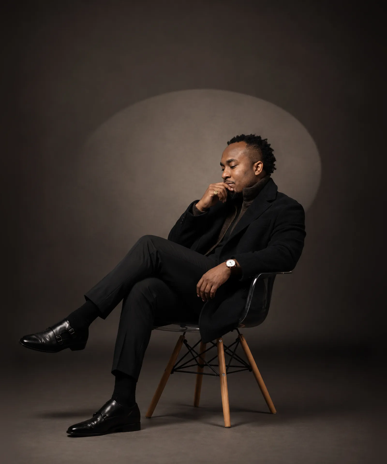 Kemal Brown seated on a chair in a spotlight, hand at his chin, eyes closed.