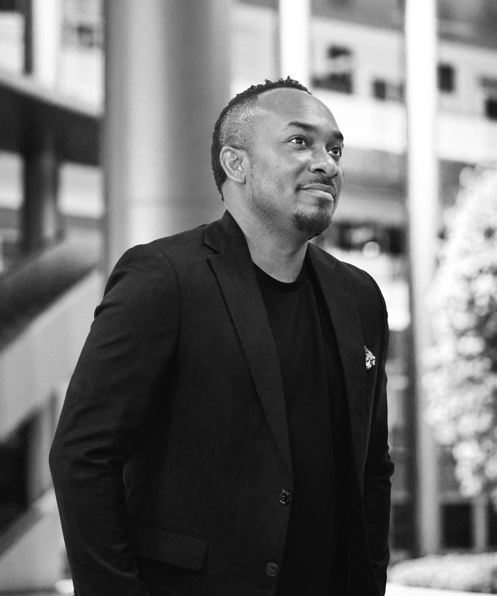 Kemal Brown in a black jacket, smiling and looking away, in black and white.