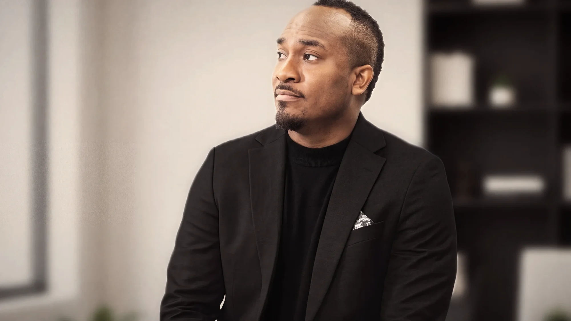 Kemal Brown in black, seated, looking off camera.
