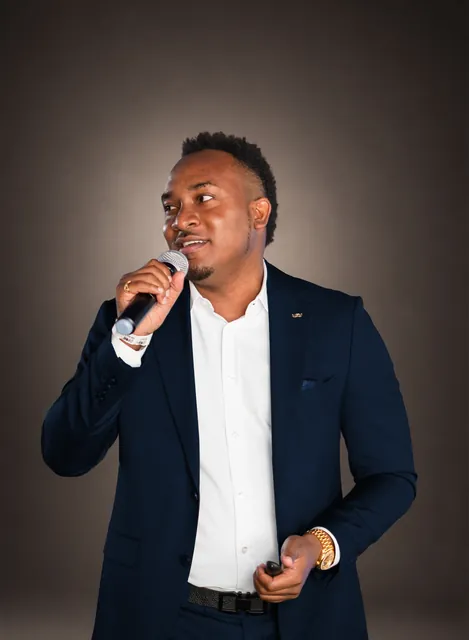 Kemal Brown in a suit and white shirt, speaking into a handheld microphone.