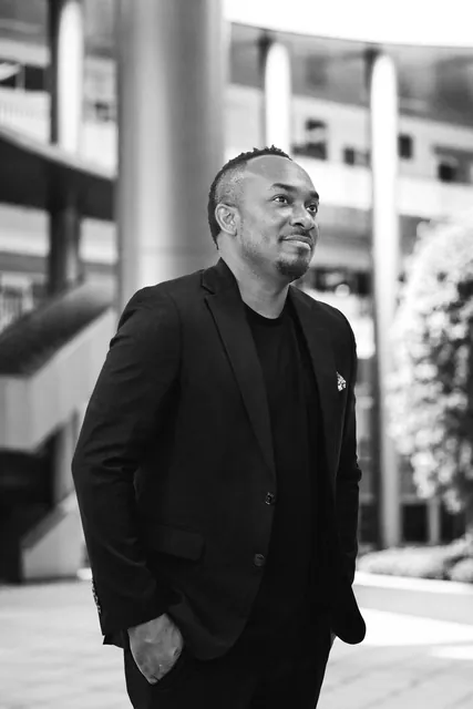 Kemal Brown in a black jacket in a city plaza, in black and white.