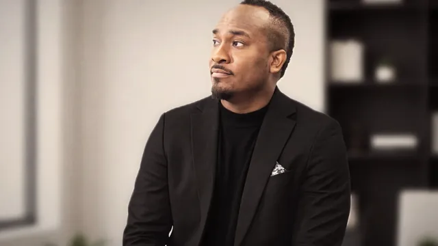 Kemal Brown in a black jacket and turtleneck, seated in an office, looking off camera.